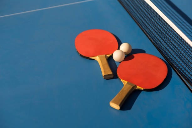 Table tennis ping pong paddles and white ball on blue board